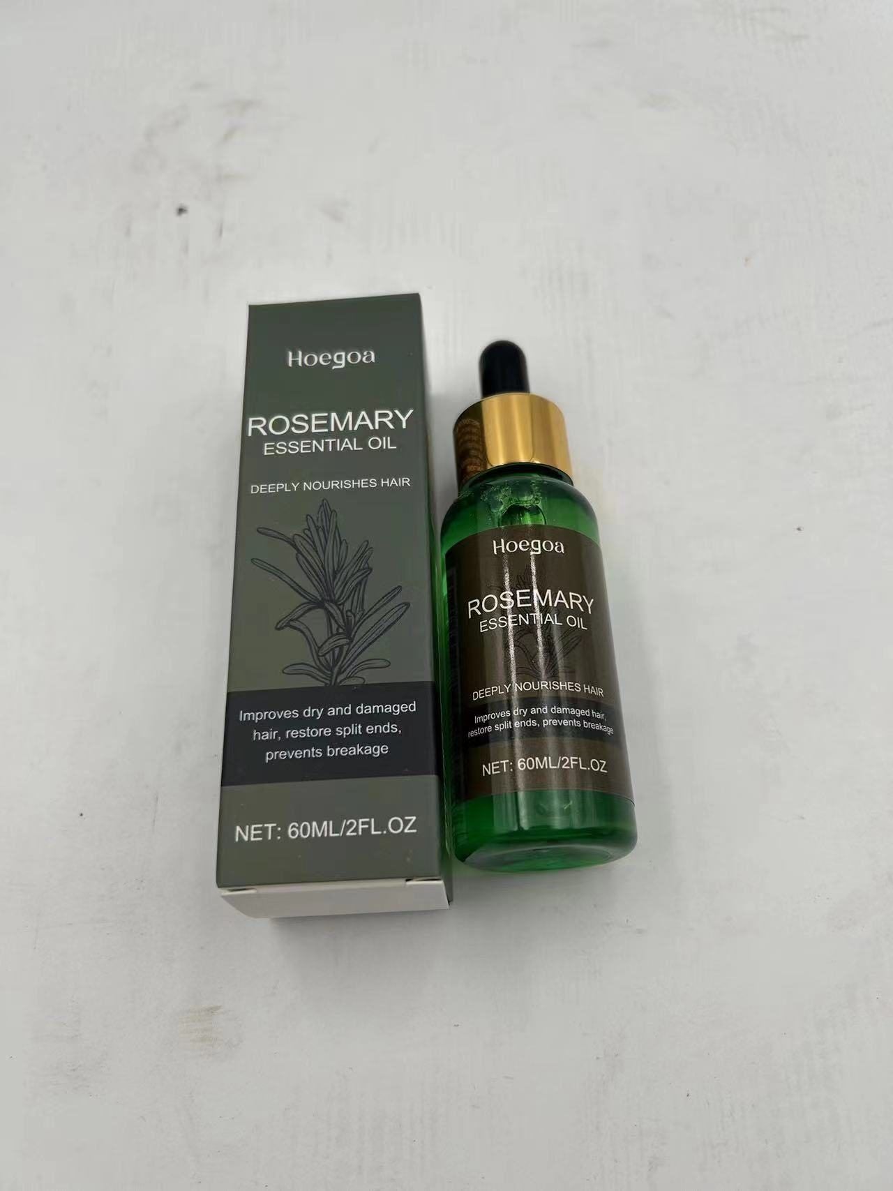 A bottle of Hoegoa Rosemary Essential Oil next to its dark gray packaging box, placed on a light gray textured surface.