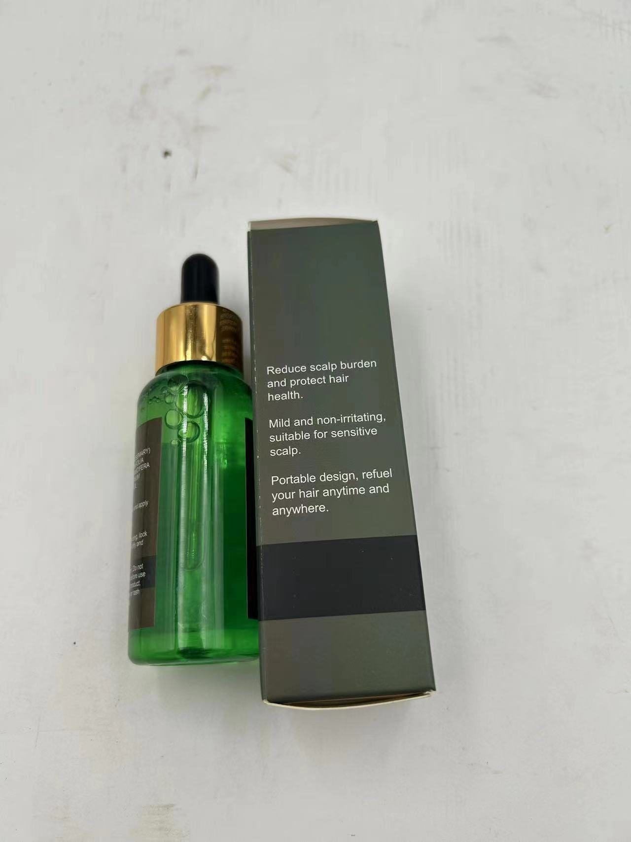 A green glass dropper bottle with a gold collar next to its dark gray and black cardboard packaging box, placed on a light off-white textured surface.