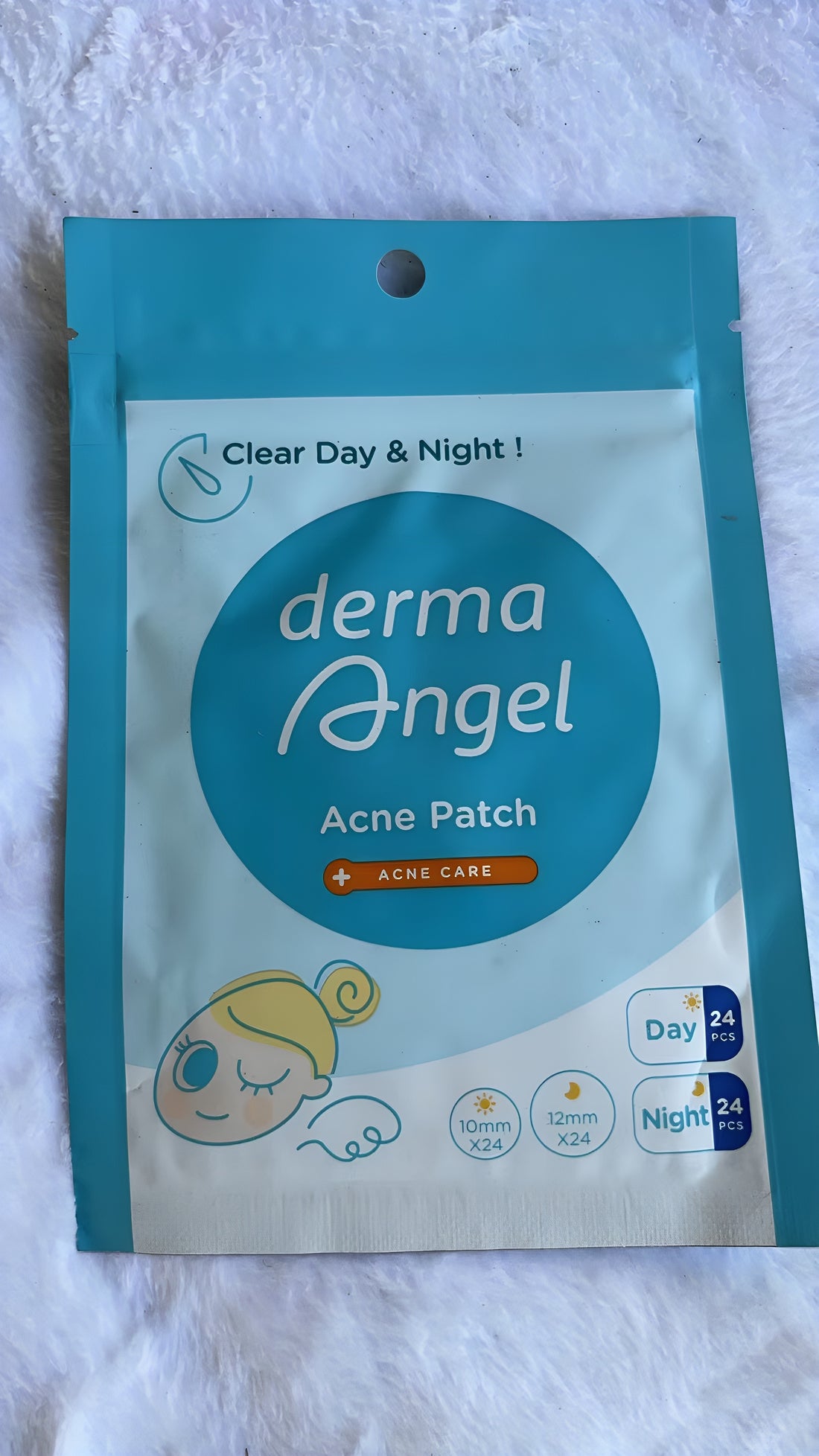 A package of derma Angel Acne Patch on a soft white textured fabric background. The packaging is teal and white with a prominent teal circle in the center containing the brand name 'derma Angel' in white script.