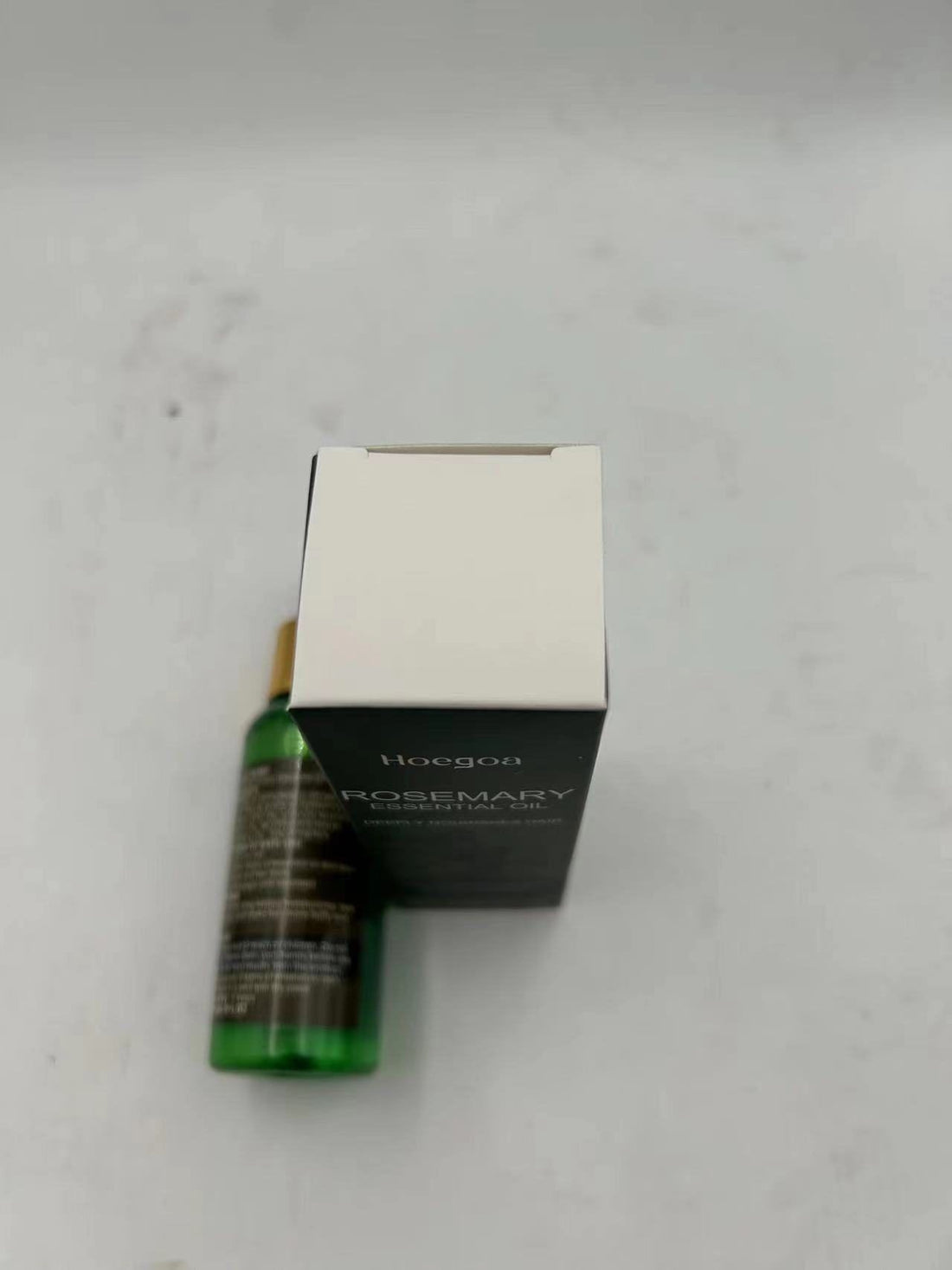 A small green bottle of Hoegh Rosemary Essential Oil next to its white and black product box on a light gray surface.