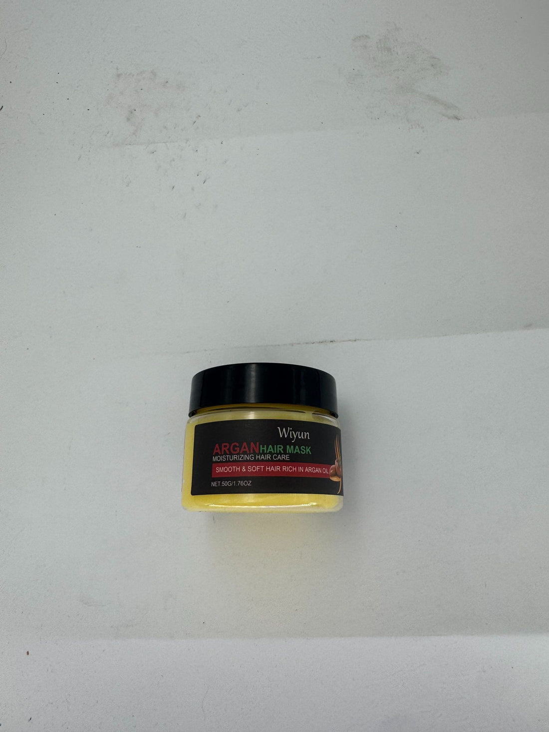 A small jar of Wiyun Argan Hair Mask moisturizing hair care, featuring a black lid and a label with yellow, red, and white text, set against a plain off-white background.