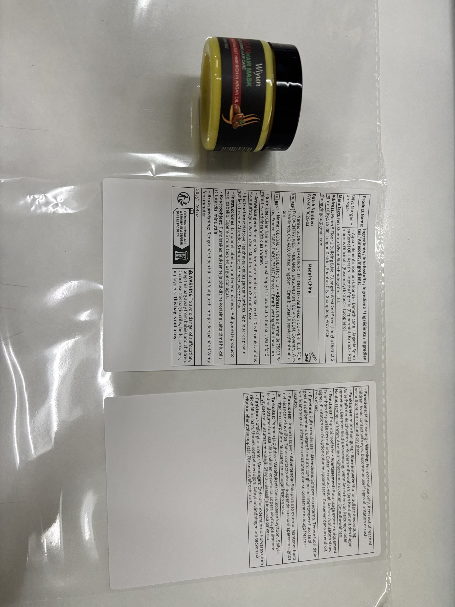 A small jar of yellow cosmetic or hair product with a black lid sits above two white instruction sheets on a clear plastic surface.