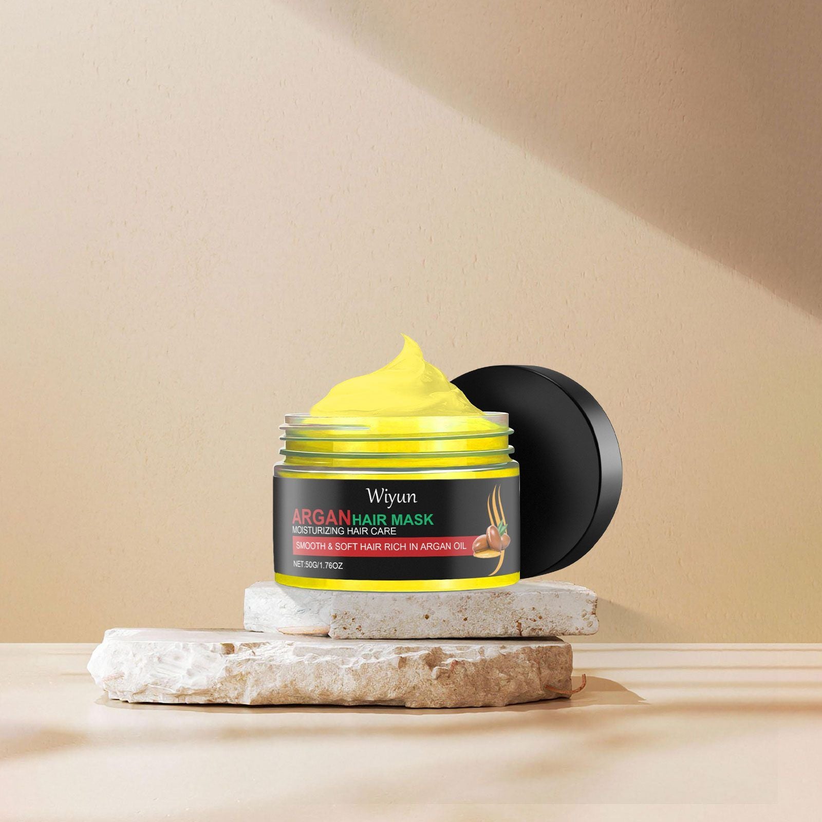 Wiyun Argan Hair Mask moisturizing hair care jar with a black lid and a bright yellow cream product, styled on stacked stone slabs against a beige background.