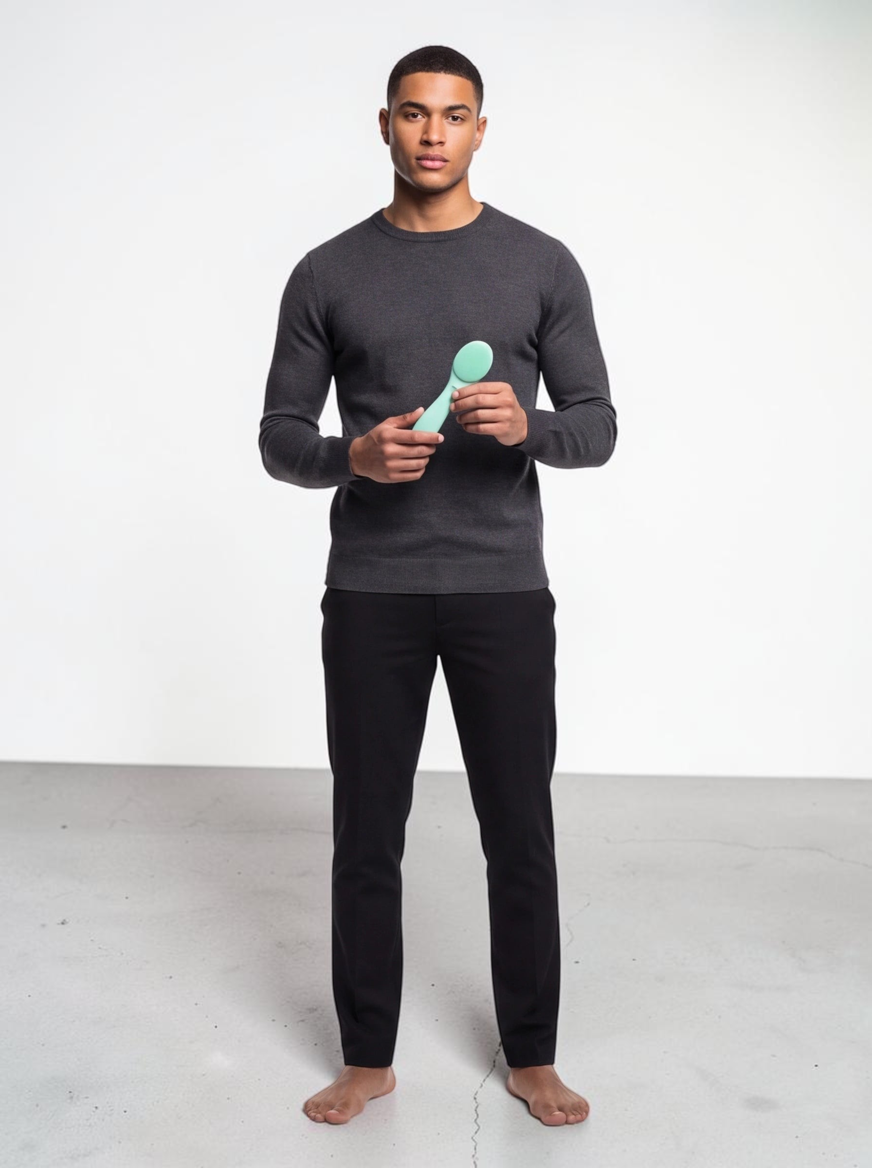 A man holding a light green TheGromify ultrasonic silicone cleansing brush against a plain white studio background.