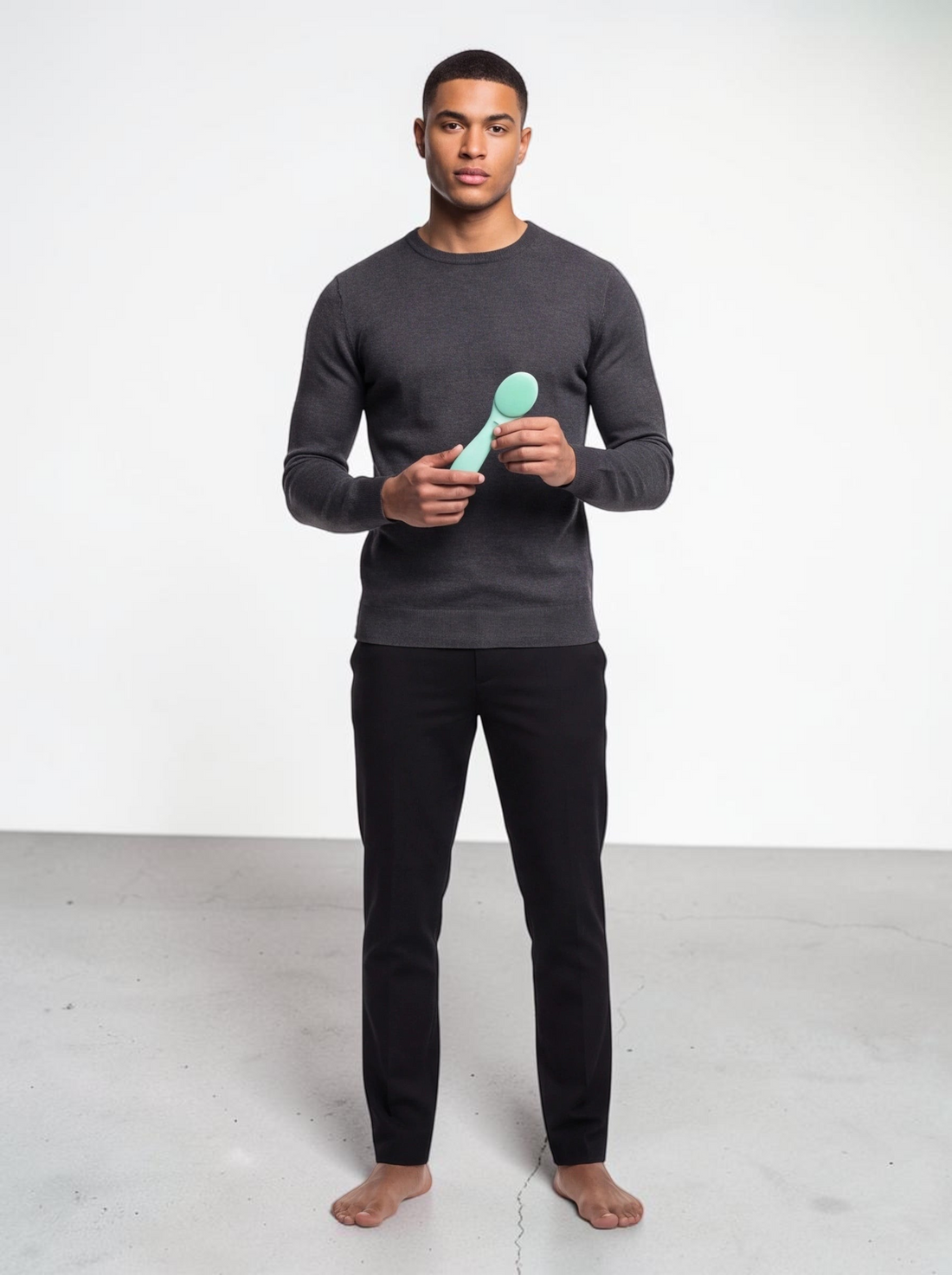 A man holding a light green TheGromify ultrasonic silicone cleansing brush against a plain white studio background.