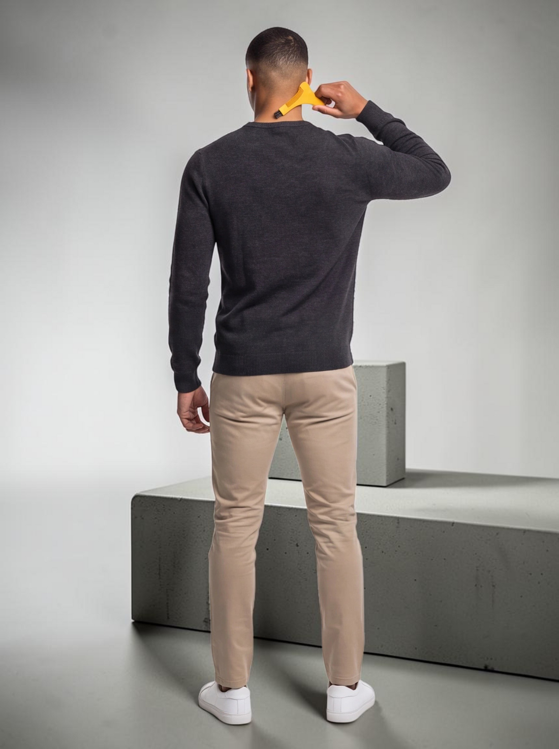 TheGromify yellow beard lining tool held by a man in a dark sweater and beige trousers against a white background