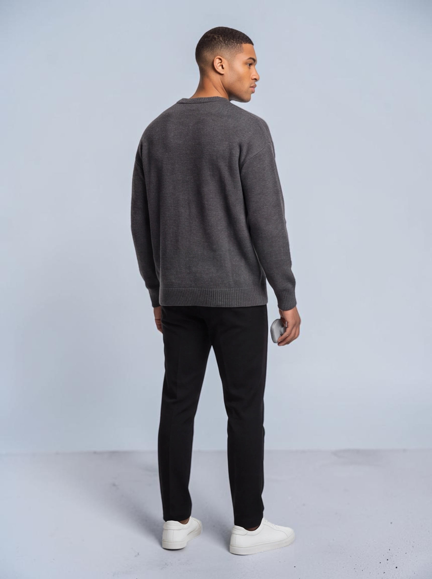 TheGromify silicone face and beard cleansing brush held by a man wearing a grey sweater and black trousers