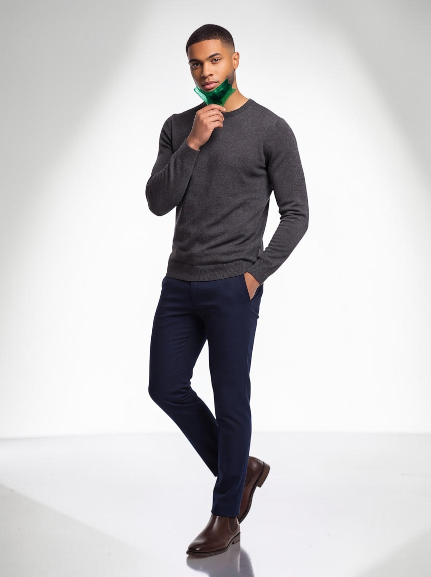 TheGromify man grooming his beard with a green wide-tooth pocket comb while wearing a grey sweater and navy trousers.