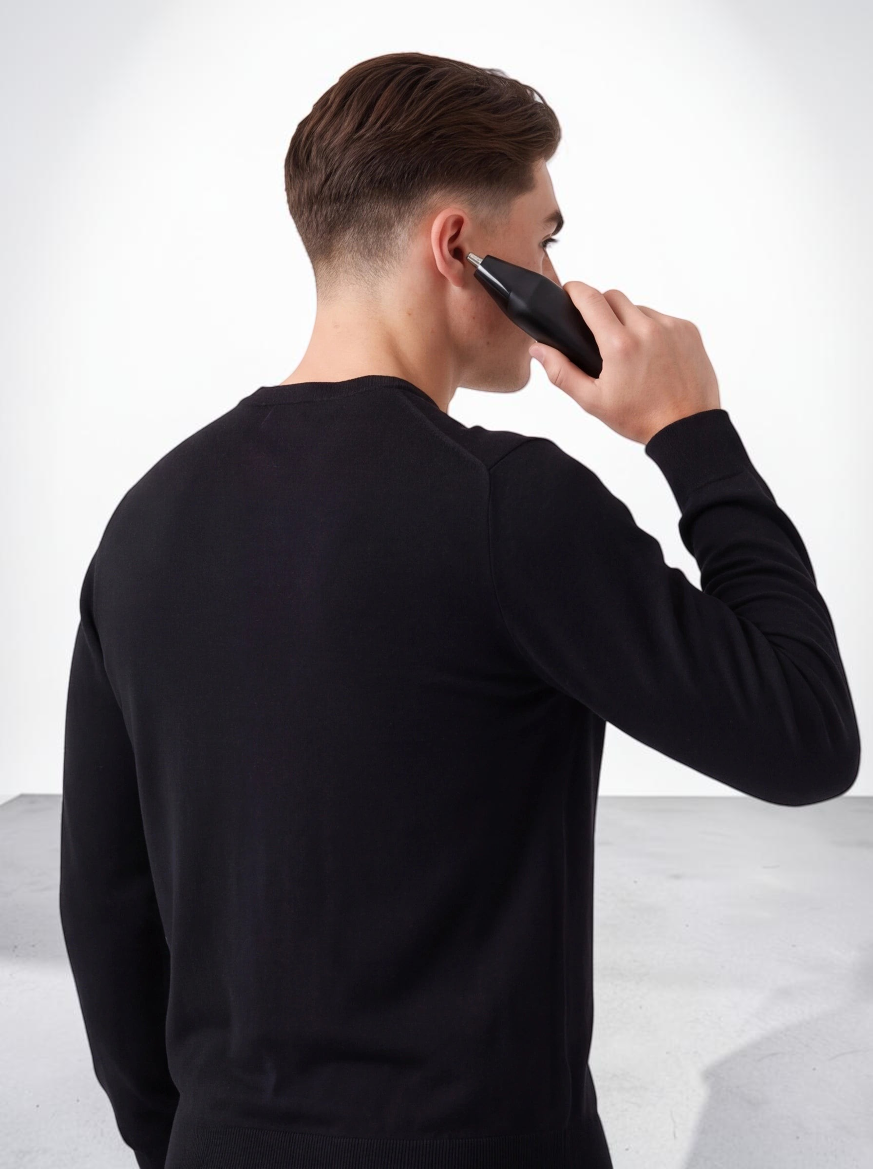 Man using a black TheGromify 3-in-1 cordless trimmer to groom ear hair against a white background
