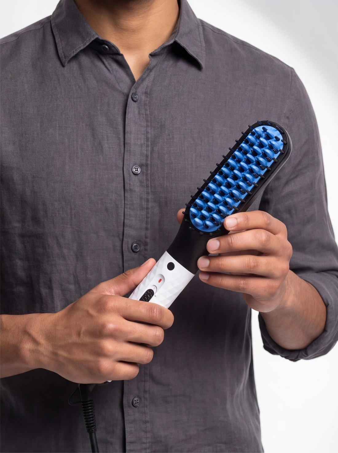 TheGromify heated beard and hair straightening comb with blue anti-scald teeth held by a man in a grey shirt