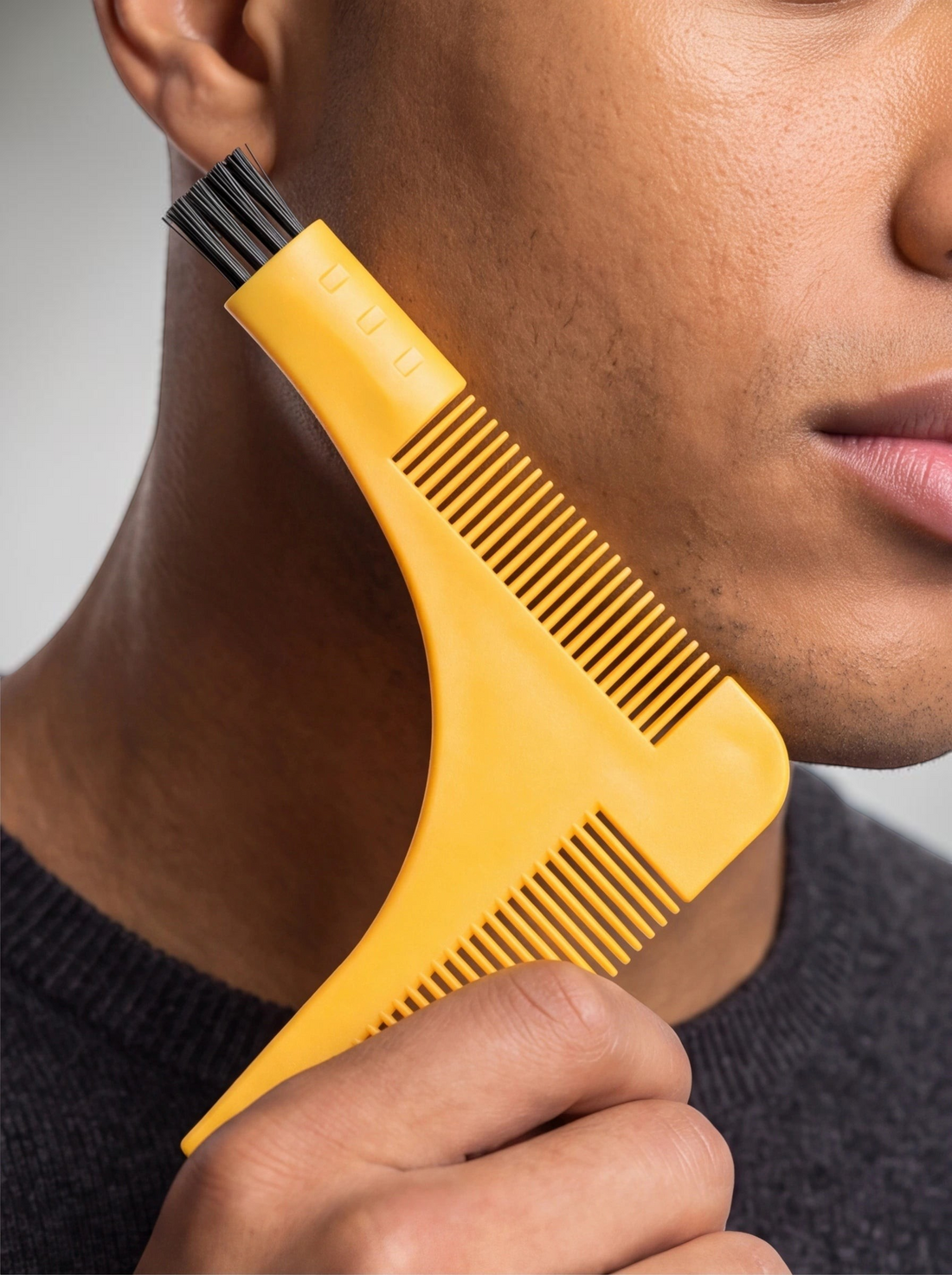 TheGromify yellow beard lining tool with integrated comb and brush being used to shape a beard on a man's cheek.