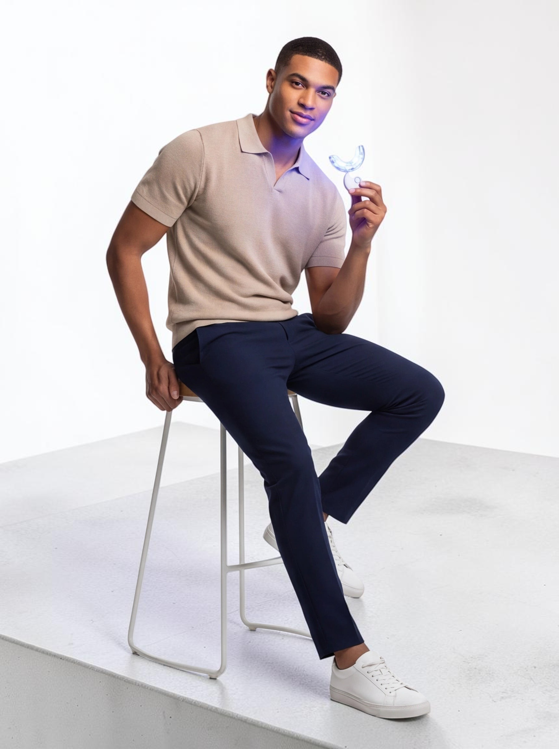TheGromify 32-LED teeth whitening kit held by a man in a beige polo shirt sitting on a stool against a white background