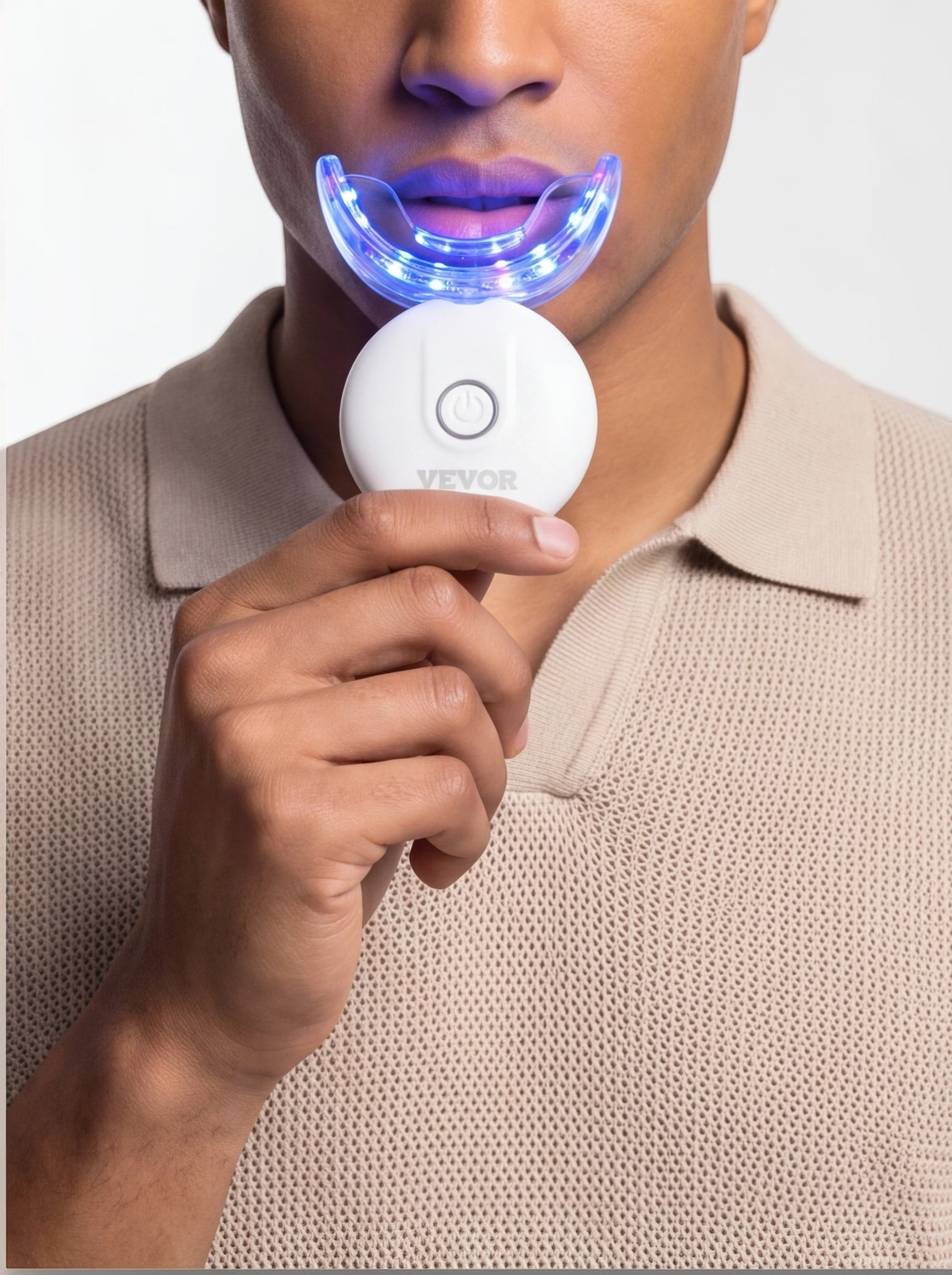 TheGromify 32-LED teeth whitening kit with a blue light tray being used by a man in a beige polo shirt.
