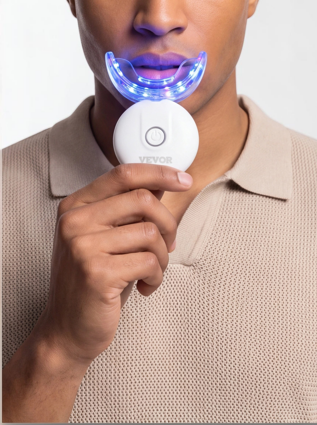 TheGromify 32-LED teeth whitening kit with a blue light tray being used by a man in a beige polo shirt.