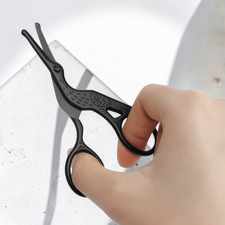 TheGromify black stork-shaped grooming scissors for precise nose and ear hair trimming held by a hand.