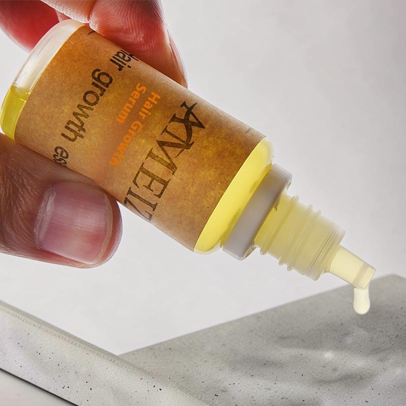 TheGromify hair growth accelerator tonic in a small amber bottle with a dropper dispensing a drop of golden serum