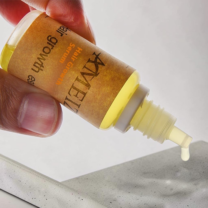 TheGromify hair growth accelerator tonic in a small amber bottle with a dropper dispensing a drop of golden serum