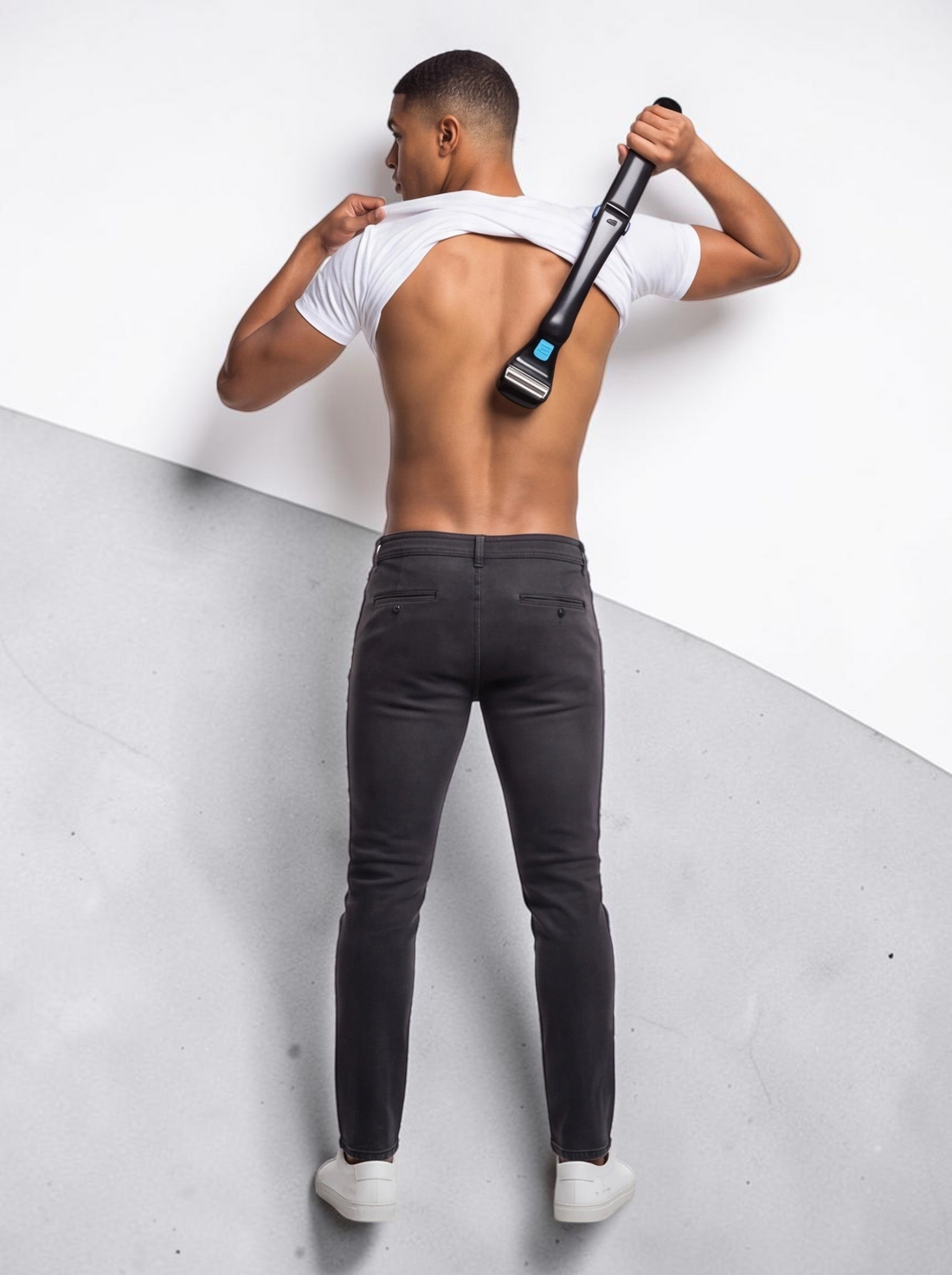 A man using a black TheGromify long-handle back hair shaver to groom his back, showing the ergonomic reach.