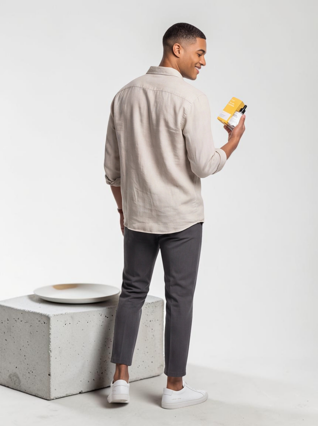 A man in a beige shirt holding a TheGromify Nicotinamide Brightening Face Serum bottle and box in a studio setting.