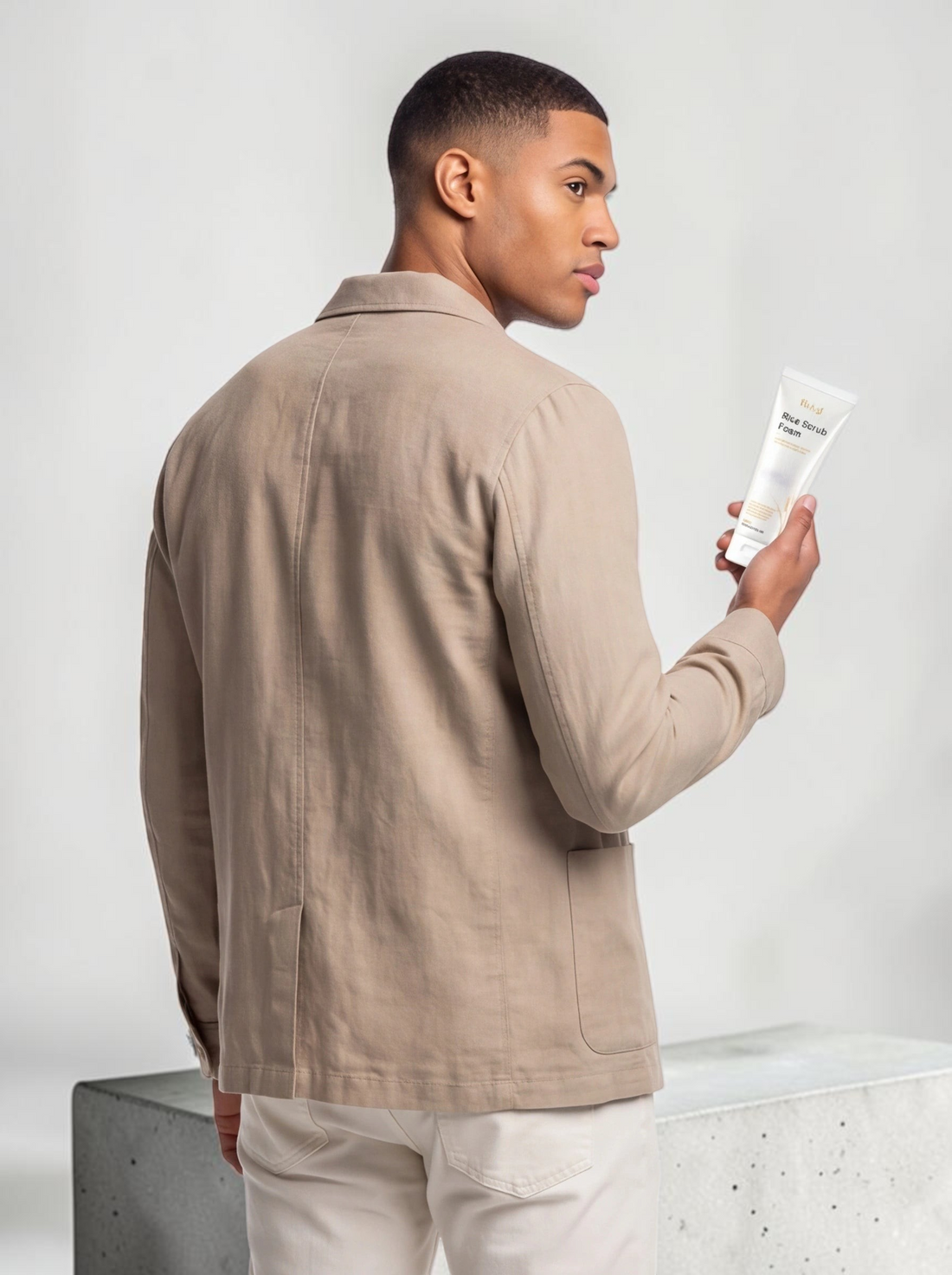 TheGromify man in a beige blazer holding a tube of Rice Water Daily Face Cleanser against a white background