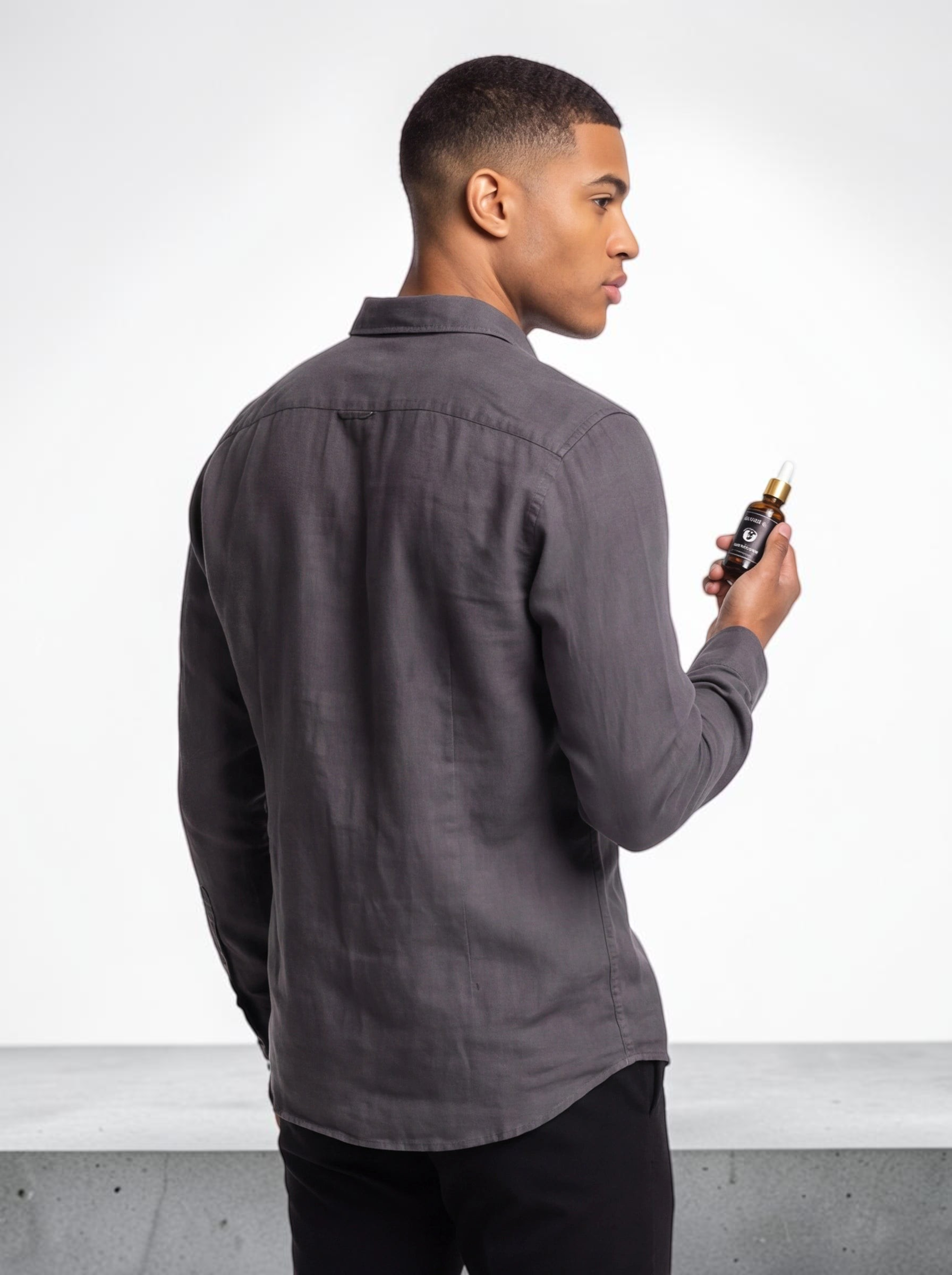 TheGromify Sandalwood & Vitamin E Beard Oil held by a man in a grey shirt in a sophisticated, dark-toned room.