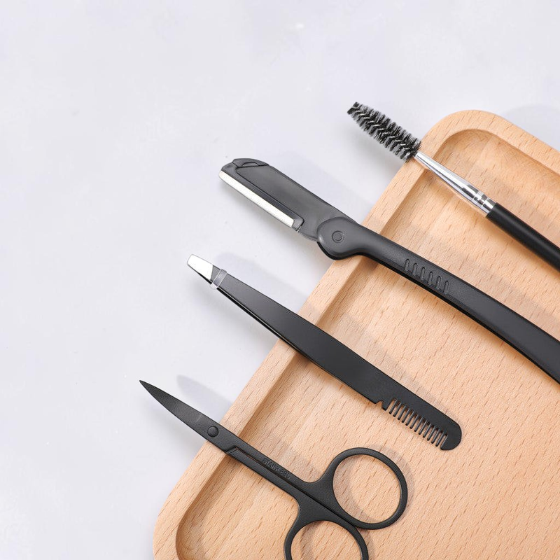 TheGromify precision eyebrow grooming kit featuring matte black stainless steel scissors, tweezers, razor, and brush.