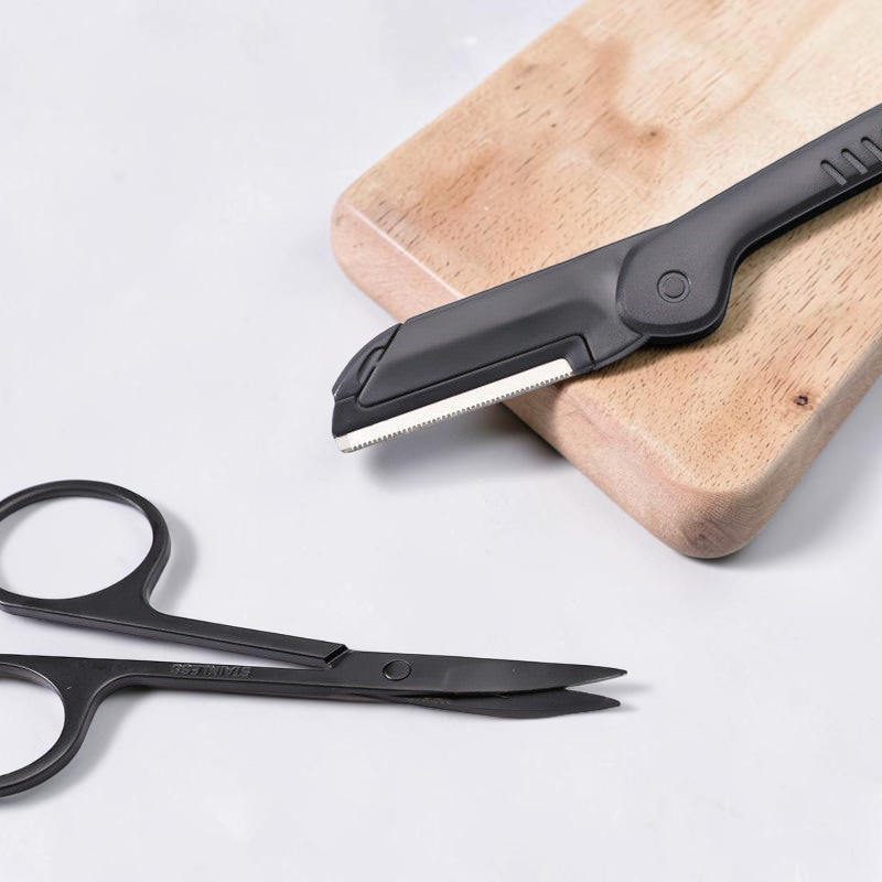TheGromify stainless steel eyebrow grooming kit featuring a black precision razor and trimming scissors on wood board