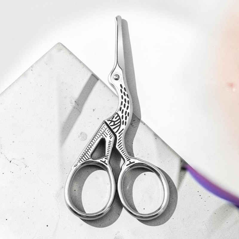 TheGromify silver stork-shaped grooming scissors for precise nose and ear hair trimming on a concrete surface.