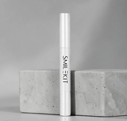 TheGromify wireless teeth whitening gel pen in white packaging standing upright on a grey stone block