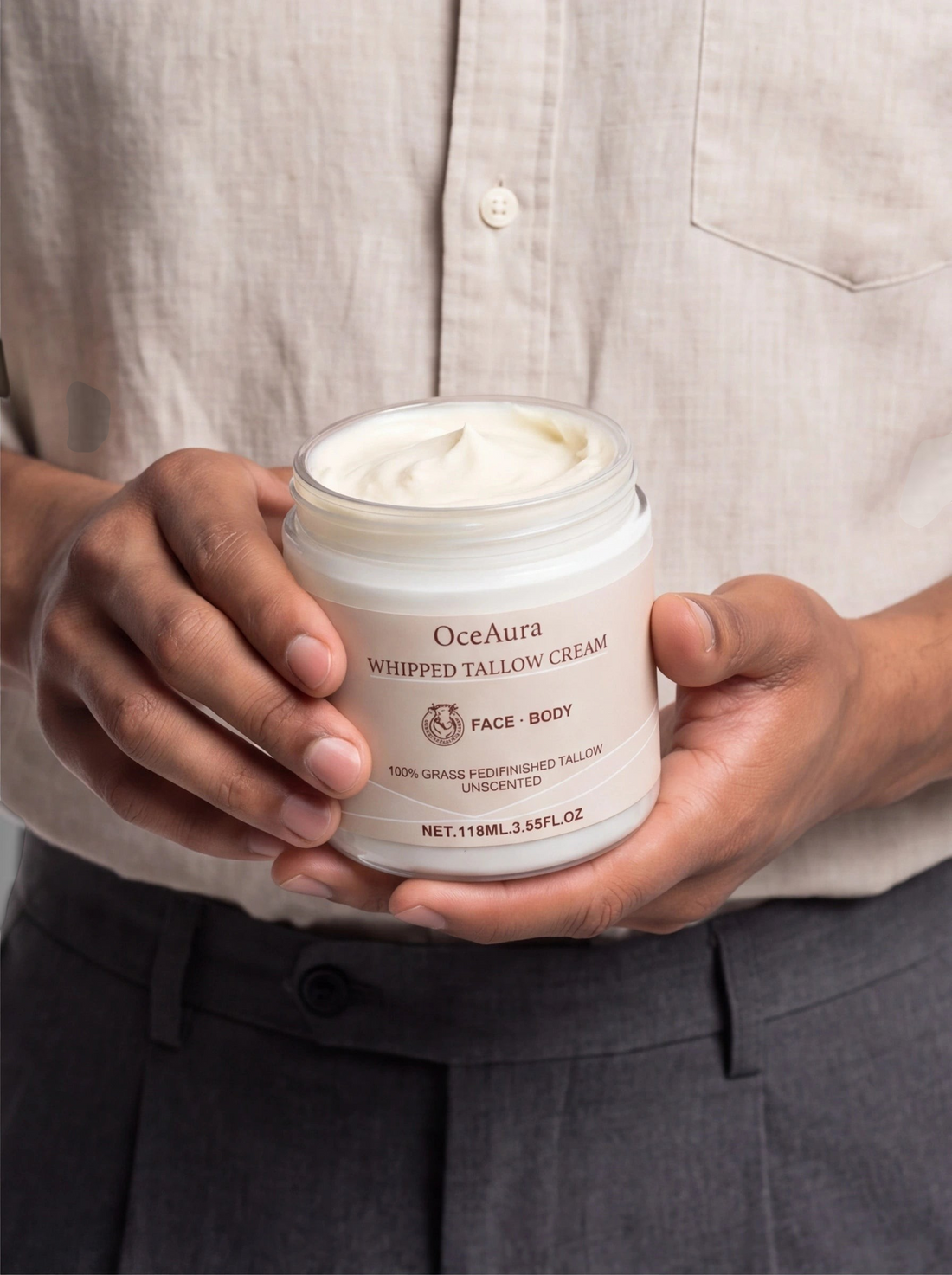 TheGromify Oceaura whipped tallow face and body cream in a white jar held by a man wearing a beige linen shirt.