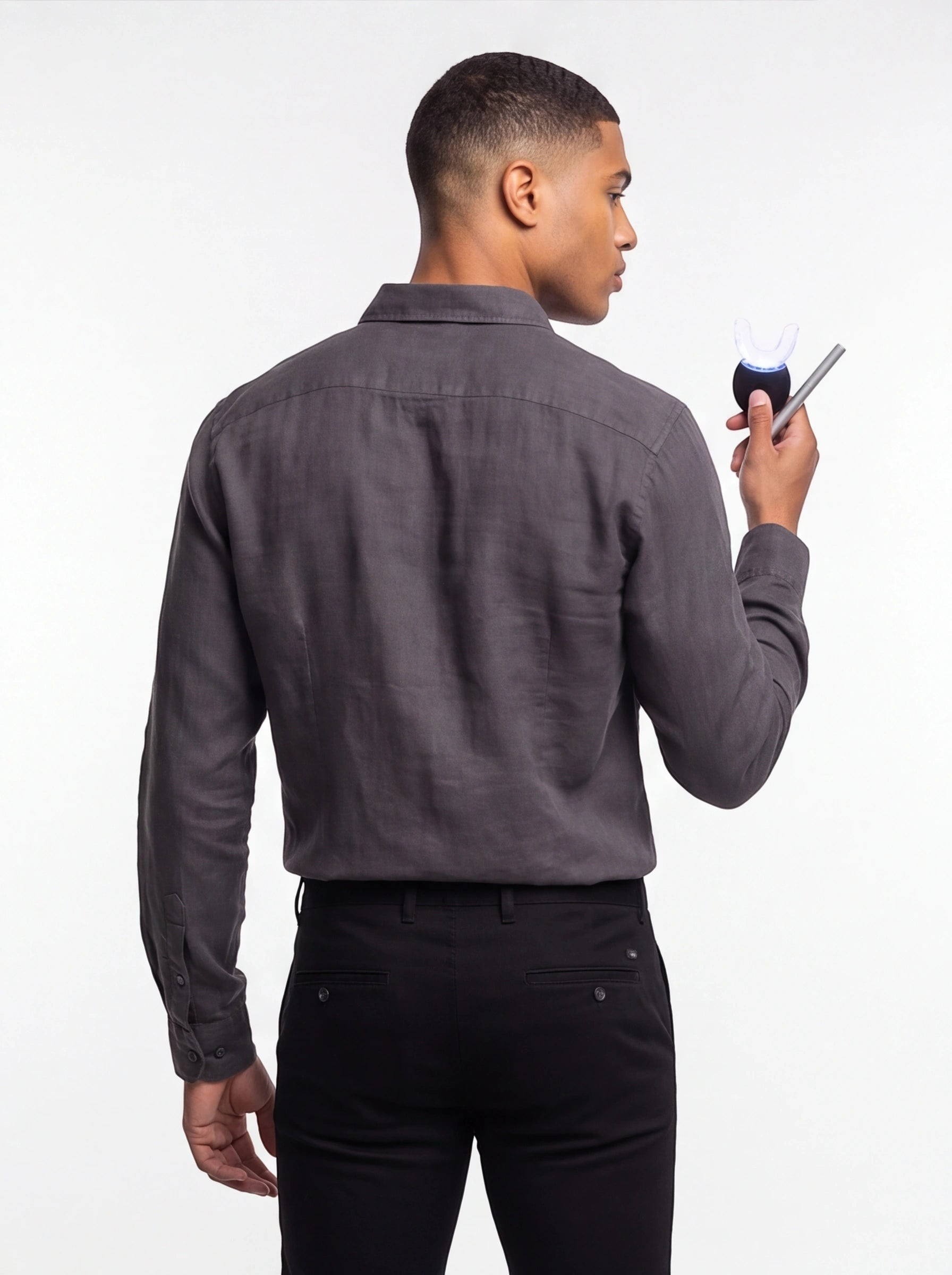 A man in a grey shirt holding a TheGromify wireless LED teeth whitening kit with a glowing blue U-shaped tray.