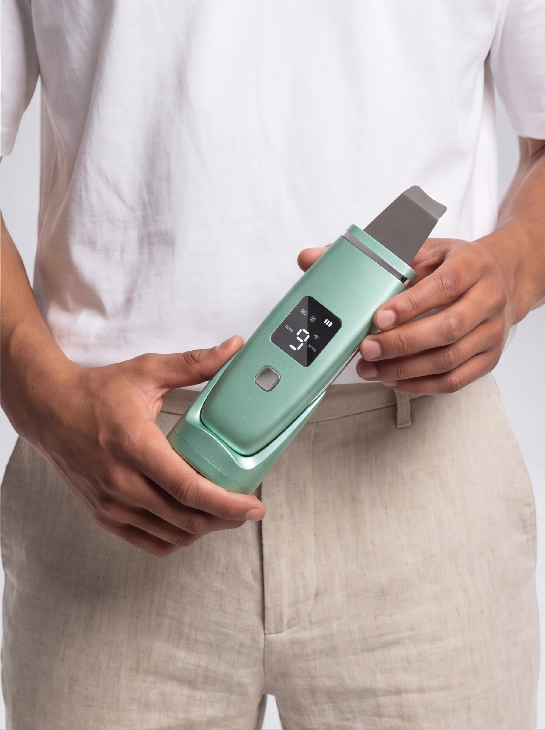 TheGromify ultrasonic skin spatula in mint green with an LED display held by a person in a white t-shirt