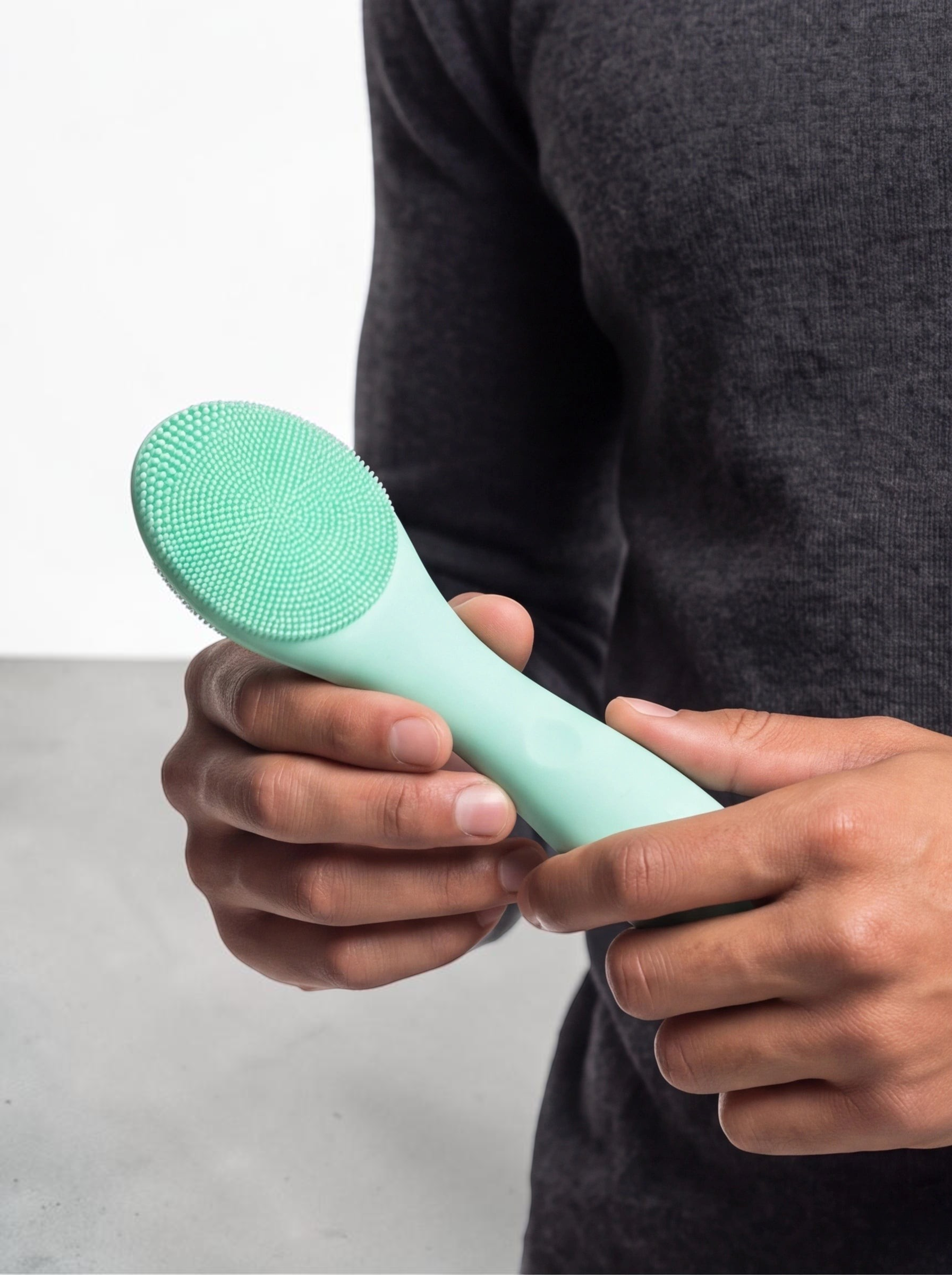 TheGromify ultrasonic silicone cleansing brush in mint green held by a man for a deep pore facial clean