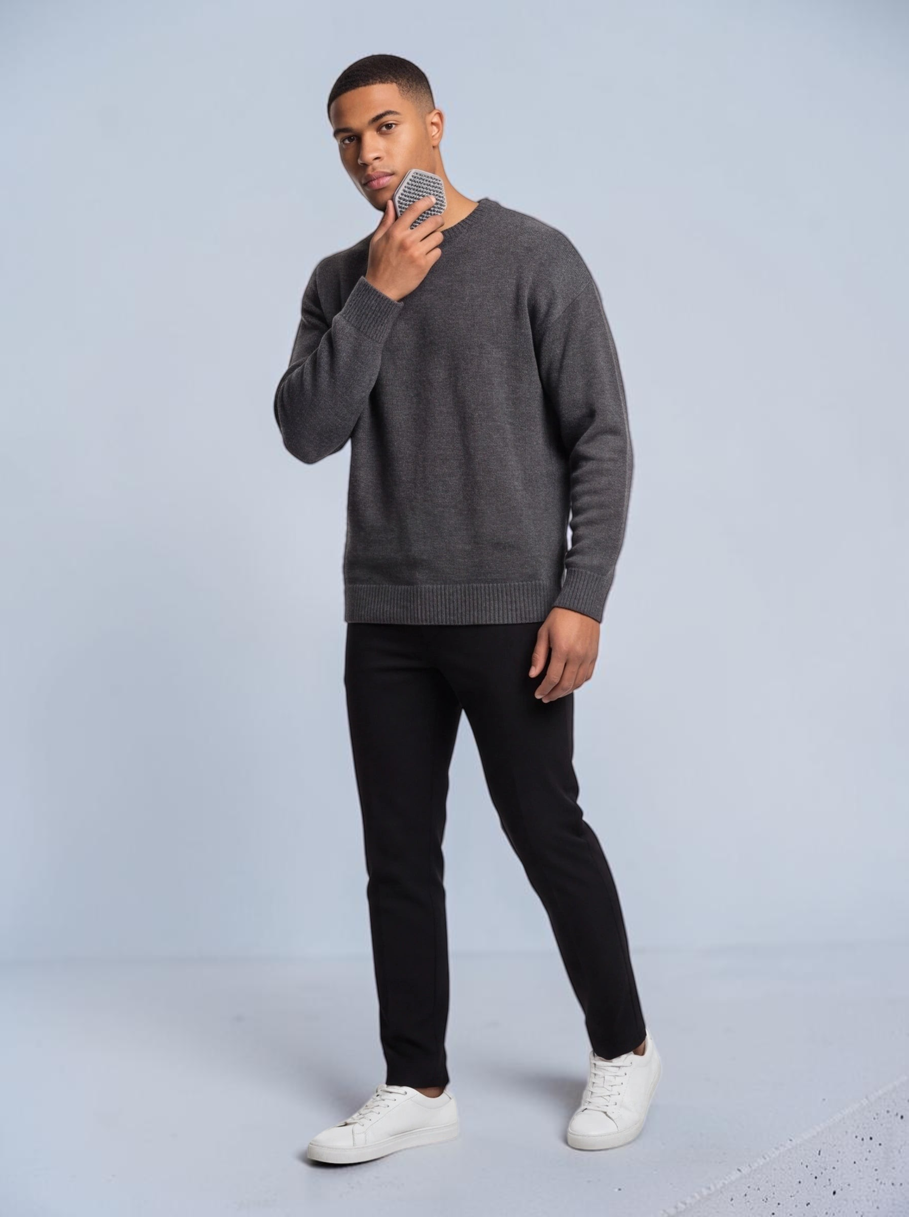TheGromify silicone face and beard cleansing brush held by a man in a grey sweater for gentle exfoliation