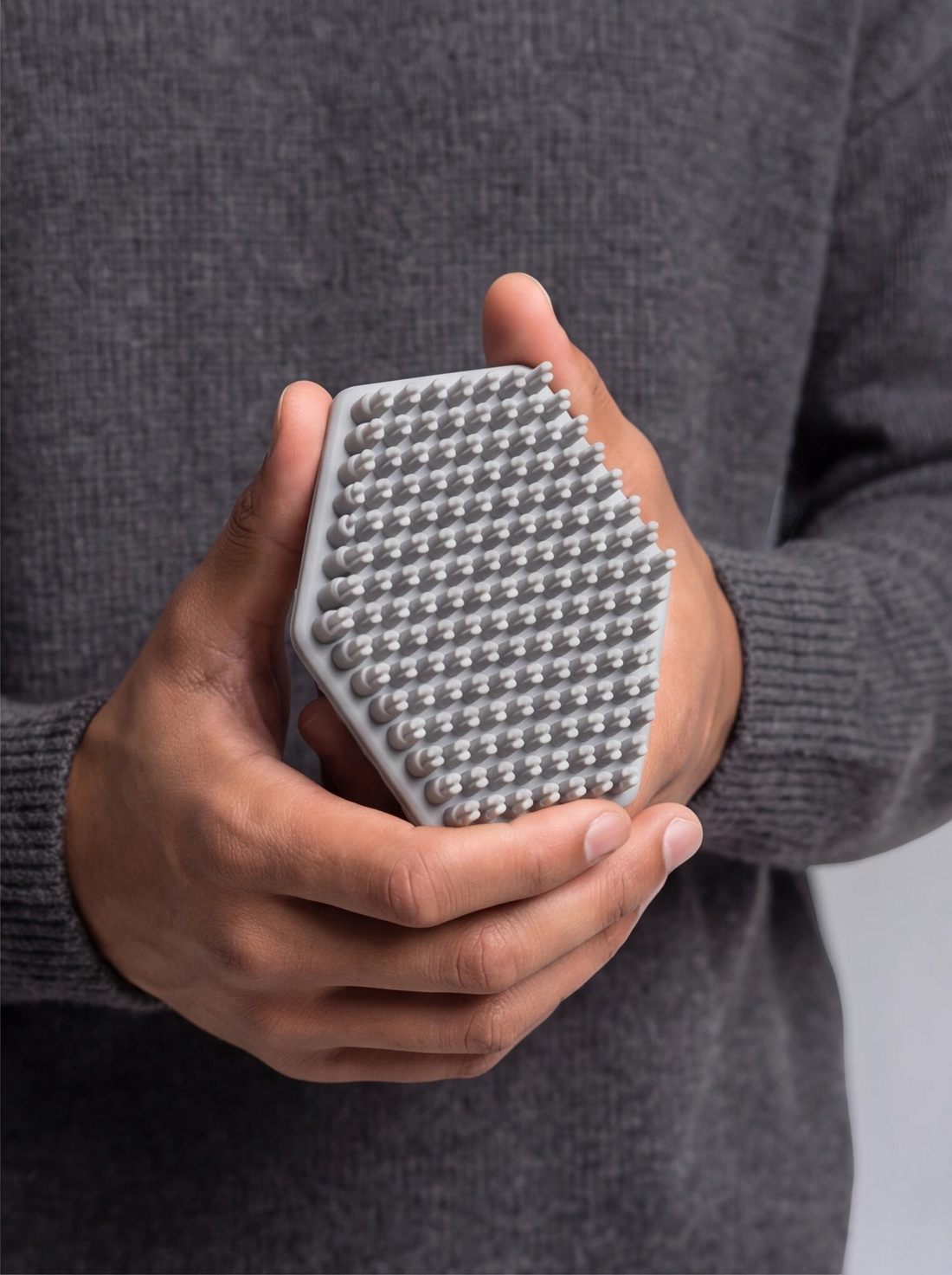 TheGromify gray silicone face and beard cleansing brush with soft bristles held in hands for gentle exfoliation.