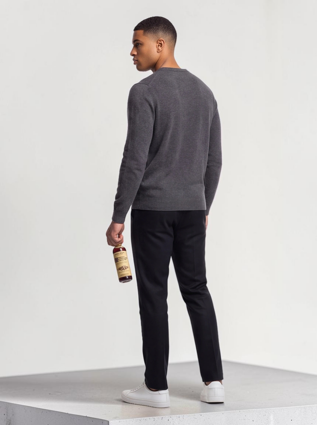 TheGromify Nourishing Beard Conditioner bottle held by a man wearing a grey sweater and black trousers
